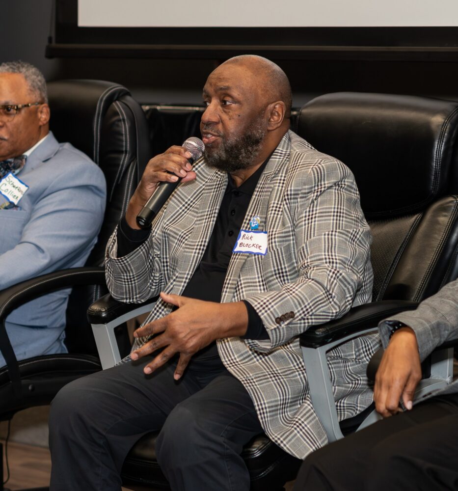 Rick Blocker in plaid blazer speaks into microphone while sitting on the panel at February's Labor in Action event.