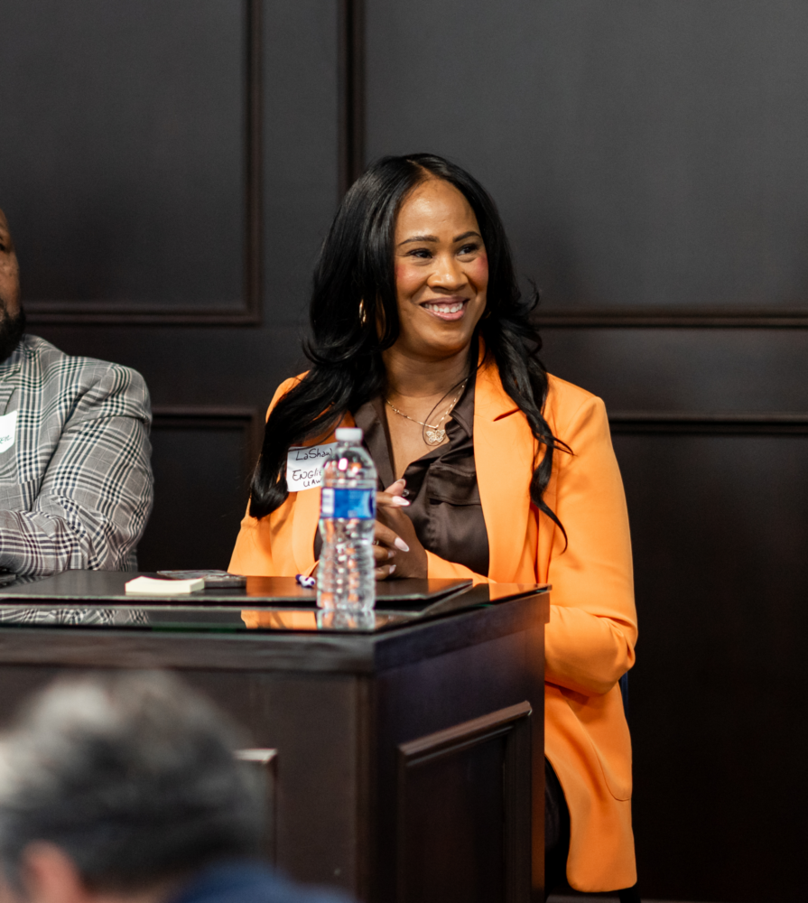 Dr. LaShawn English smiles in a bright orange blazer on the panel of a Labor in Action event.
