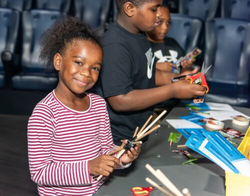 Student smiles while crafting a wooden wheel.