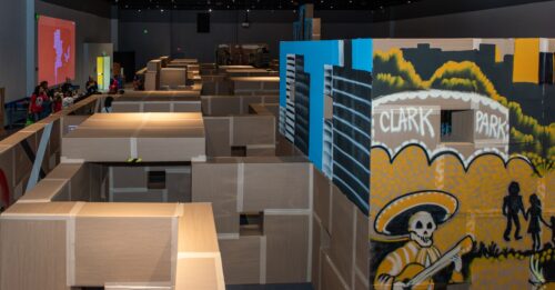 Aerial view of cardboard maze reveals paintings of a Clark Park Mural and the city skyline.