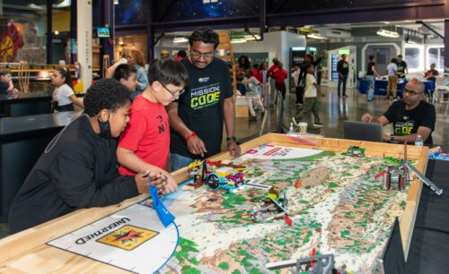 Volunteers help students build on a table with a map.