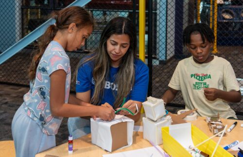 Volunteer helps students build a robot out of cardboard, pipe cleaners and felt.